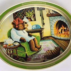May include: An oval metal tray with a green border featuring a cozy illustration. A bear in pajamas and a nightcap sits in a green armchair near a fireplace. A cat sits on a rug. The tray is labeled "Sleepytime Herb Tea."