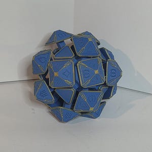 May include: A blue geometric puzzle toy with gold-colored accents. The puzzle is spherical, composed of multiple interlocking pieces, each with a unique design. The toy is designed with a complex, multi-faceted structure.