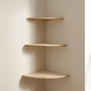 Może przedstawiać: Trzy jasne, drewniane półki narożne zamontowane na ścianie w neutralnym odcieniu. Półki są półokrągłe, z naturalnym wykończeniem słojów drewna. Półki są rozmieszczone, tworząc minimalistyczny i funkcjonalny design.