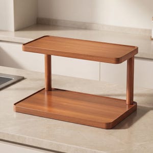 Pode incluir: Uma prateleira de madeira de dois níveis em forma retangular com bordas arredondadas. A prateleira é feita de madeira de tom médio quente e é suportada por quatro pernas cilíndricas. A prateleira é projetada para armazenamento e exibição.