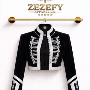 May include: A black cropped jacket with white trim and silver-coloured embellishments. The jacket features a high collar and long sleeves. The brand name "ZEZEFY APPAREL CO." is displayed above the jacket.