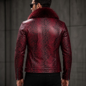 Peut inclure: Une veste rouge fonc&eacute; avec un motif peau de serpent noir sur toute la surface, un col en fausse fourrure rouge fonc&eacute; pro&eacute;minent et des manches longues avec des poignets zipp&eacute;s. La veste est port&eacute;e avec un pantalon noir et des lunettes.