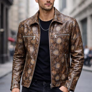 以下が含まれることがあります： 茶色とタン色のヘビ柄レザー ジャケット。襟付きで、シルバーのジッパーが付いています。黒いTシャツの上に着用し、黒いジーンズと合わせています。シルバーのチェーンネックレスが見えます。