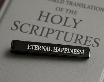 May include: A black tie clip with the words "ETERNAL HAPPINESS!" in white lettering, resting on a gray book titled "NEW WORLD TRANSLATION OF THE HOLY SCRIPTURES."