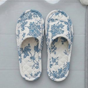 以下が含まれることがあります： 青と白の花柄のオープントゥスリッパのペア。 スリッパはキルティングデザインで、柔らかくクッション性のあるインテリアを備えており、屋内での使用に最適です。 快適さとリラックスのために設計されています。