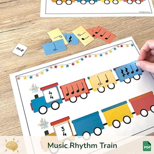 May include: A colorful music rhythm train educational game with a blue locomotive and various train cars. The game includes musical notes and numbers, with the text "Music Rhythm Train" at the bottom. A hand is placing a musical note on the train.