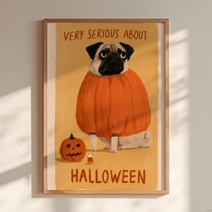 May include: A framed wall art print featuring a tan pug wearing a large, textured orange jumper. The illustration includes a small jack-o'-lantern and a piece of candy corn, with the text "VERY SERIOUS ABOUT HALLOWEEN" printed in brown.