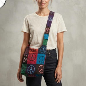 May include: A crossbody bag featuring a patchwork design of square fabric panels in various colors including red, blue, green, and purple. Each panel is printed with a circular peace sign symbol in a contrasting color. The bag has a wide shoulder strap.