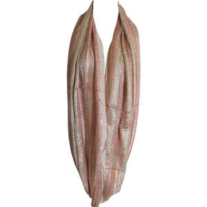 May include: An infinity scarf featuring a vertical striped pattern in alternating shades of metallic gold and soft peach. The fabric has a textured, woven appearance with a subtle shimmer throughout the entire length of the garment, creating a continuous loop design that hangs in soft, draped folds.
