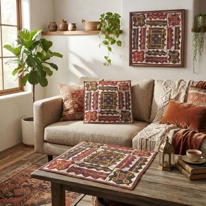 May include: A square textile wall hanging and a matching square throw pillow featuring a patchwork design in shades of deep red, brown, and cream with intricate embroidery and small mirror accents, displayed in a living room setting.
