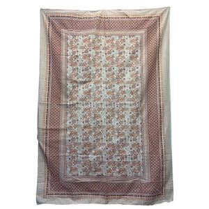 May include: A rectangular, cream-colored textile with a floral pattern in shades of orange and brown. The border features a geometric design in burgundy and cream. The textile is likely a tablecloth or a decorative fabric.
