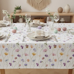 May include: A set of three ceramic mugs with a speckled, cream-colored glaze. Each mug features a different hand-painted design: a blue and green leaf, a yellow flower, and a red berry. The mugs have a simple, rounded shape.