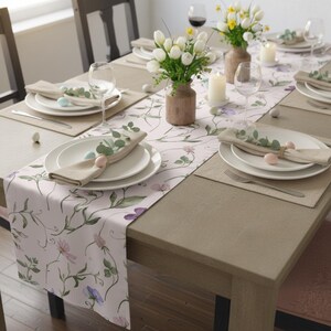 Peut inclure: Une table de salle &agrave; manger dress&eacute;e pour une c&eacute;l&eacute;bration printani&egrave;re. La table est orn&eacute;e d'un chemin de table floral, d'assiettes blanches, de serviettes beiges et d'&oelig;ufs de P&acirc;ques aux couleurs pastel. Des vases de tulipes blanches et des bougies compl&egrave;tent l'ambiance festive.