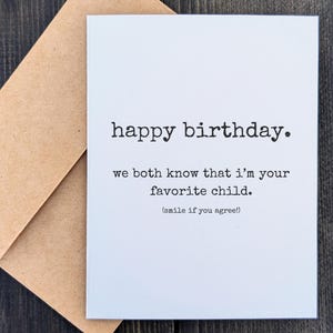 May include: A white greeting card with the text "happy birthday." and the message "we both know that I'm your favorite child. (smile if you agree!)" is paired with a brown envelope.