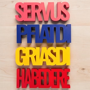 Pode incluir: Letras de madeira vermelhas, azuis e amarelas soletrando as palavras "SERVUS", "PIATDI", "GRIASDI" e "HABEDERE". As letras estão dispostas horizontalmente sobre uma superfície de madeira clara.