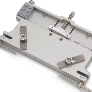 May include: A silver metal tool with adjustable components, including screws and gray rubber pads. The tool has the text "Rick Design and Quality" and measurements of 5/64 and 1/16.
