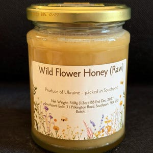 May include: A jar of Wild Flower Honey (Raw) with a gold lid. The label states the honey is from Ukraine, packed in Southport, and weighs 340g. The label includes floral illustrations and the text "BB End Dec. 2027".