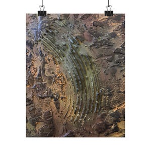 May include: Abstract art print featuring a textured, multi-toned surface with a curved, ribbed design. The artwork displays shades of brown, gold, and gray, creating a sense of depth and dimension. The print is held by two black binder clips.