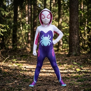 May include: A full-body hooded jumpsuit costume featuring a white hood and sleeves, a purple torso and legs, and a light blue spider emblem on the chest. The design includes pink web patterns on the sides and white eye masks with pink outlines.