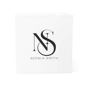 May include: A white square product box featuring a black monogram of the letters "NS" and the name "Nicole Smith" in a minimalist, elegant design. The logo is centered on the box.