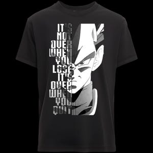 Peut inclure: T-shirt noir avec un graphisme en niveaux de gris représentant le visage d'un personnage d'anime. Le texte "IT'S NOT OVER WHEN YOU LOSE IT'S OVER WHEN YOU QUIT" est empilé verticalement.