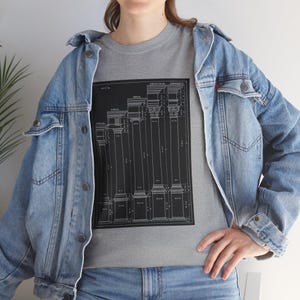 May include: A gray t-shirt featuring a black and white architectural diagram of columns. The shirt is worn with a light blue denim jacket and jeans. The diagram includes the words "Corinthian" and "Composite".