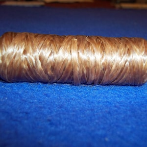 May include: A cylindrical object made of woven, light brown material. The texture appears to be fibrous and tightly packed, with a slight sheen. The object is resting on a blue surface.