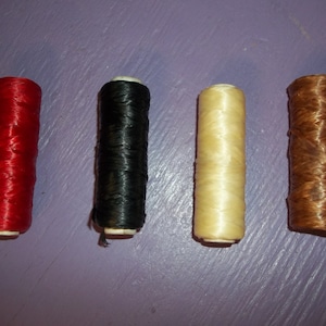 May include: Four spools of thread in red, black, cream, and brown. The spools are cylindrical and appear to be made of a tightly wound, glossy material. The thread is likely used for crafts or sewing.