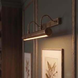 Adjustable antique brass picture lamp highlighting framed wall art with warm LED lighting.