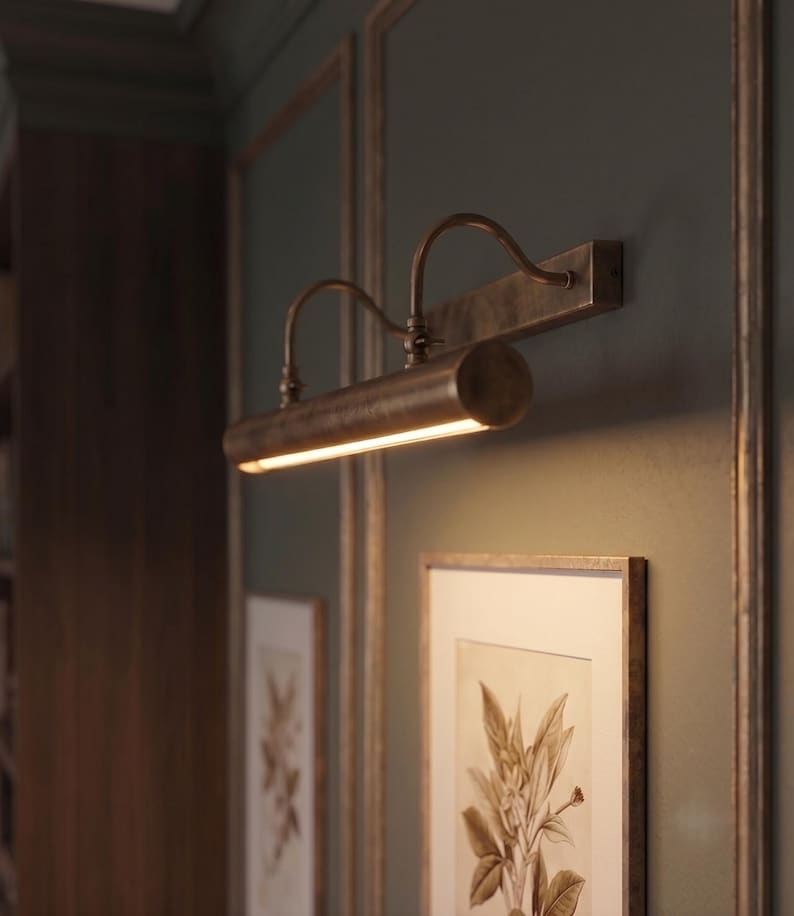 Adjustable antique brass picture lamp highlighting framed wall art with warm LED lighting.