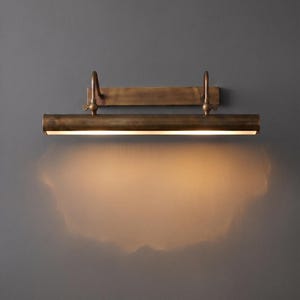 Antique patina brass picture light illuminating framed botanical artwork in elegant living room.