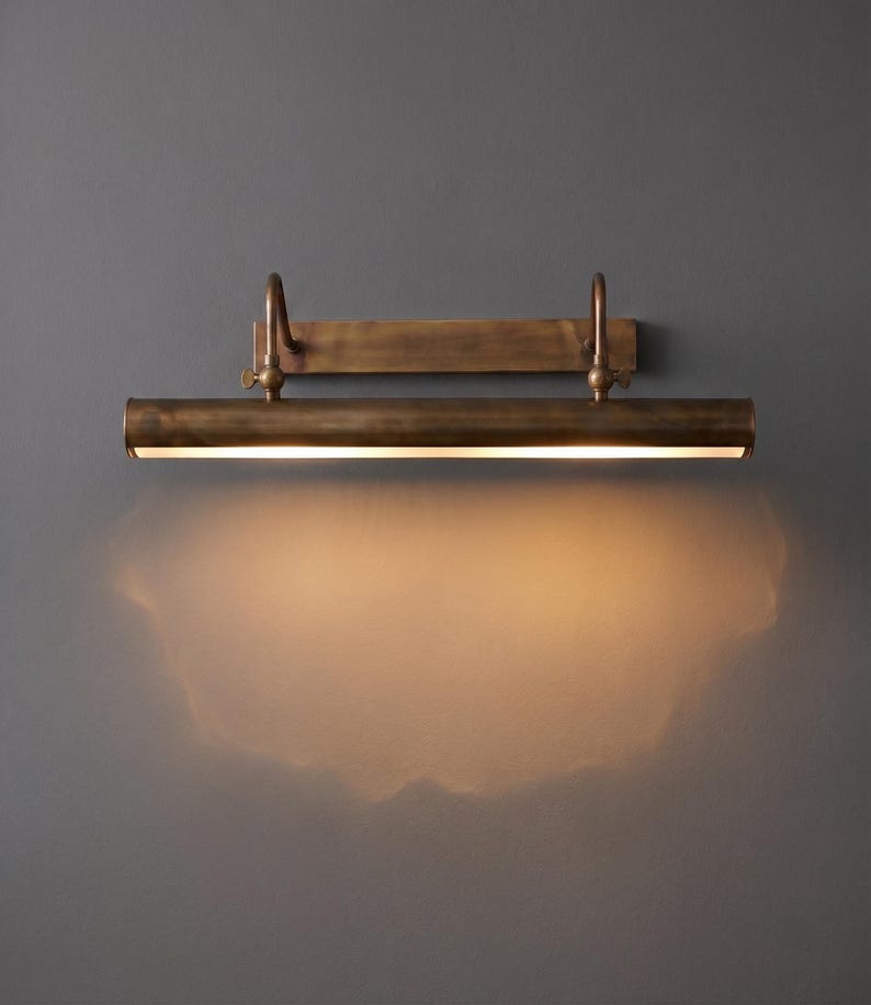 Antique patina brass picture light illuminating framed botanical artwork in elegant living room.