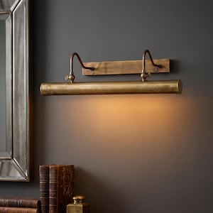 Vintage brass gallery wall light installed above artwork in luxury home office library.