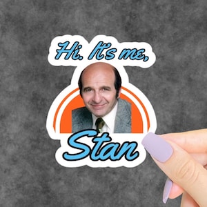 Puede incluir: Una pegatina troquelada con el retrato fotográfico de un hombre con americana gris y camisa blanca, sobre un semicírculo naranja brillante. El texto "Hi. It's me," aparece en azul claro arriba y "Stan" en azul claro abajo.