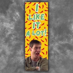 May include: A rectangular bookmark featuring a yellow background with a repeating pattern of small red chili peppers. The text "I LIKE IT A LOT!" is printed in large green letters. Below the text is a photographic image of a man with a wide expression.