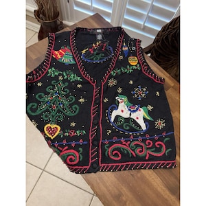 May include: Black Christmas vest with red trim and button closure. The vest features embroidered holiday designs, including a Christmas tree, rocking horse, snowflakes, and ornaments. The vest has a V-neck and is made of a knit material.