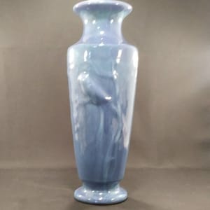 May include: A tall, blue ceramic vase with a swirling design and a bird-like figure in relief. The vase has a wide base and a narrow neck.