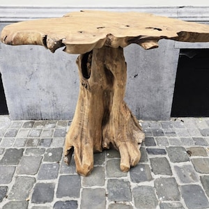 May include: A natural wood table with a unique, organic design. The tabletop is a light brown, irregular shape, supported by a textured, tree trunk-like base. The table is approximately 40 inches long and 20 inches wide.