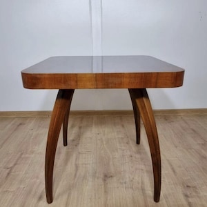 May include: A vintage wooden side table with a square top and curved edges. The table has four curved legs. The wood has a warm, brown tone. The table is likely from the mid-century modern era.