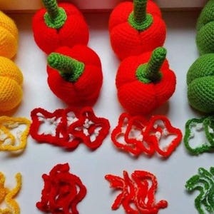 May include: A collection of handmade crochet bell peppers in yellow, red, and green. The peppers have green stems and are accompanied by crocheted pepper slices in matching colors. The arrangement is on a white surface.