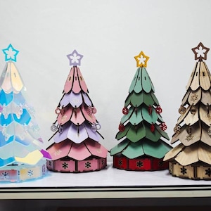 Könnte beinhalten: Vier dekorative Weihnachtsbäume aus Holz, jeder mit einem Stern. Die Bäume sind in verschiedenen Farben gehalten: schillernd, rosa, grün und Naturholz. Jeder Baum hat ein einzigartiges Design und ist ideal für die Weihnachtszeit.