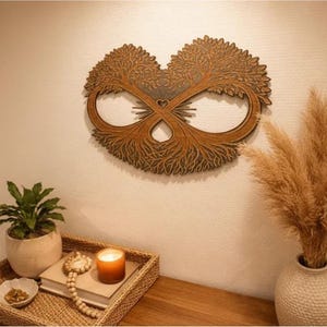 May include: A wooden wall art piece in the shape of two trees forming an infinity symbol. The artwork is brown and hangs on a cream-colored wall. A small potted plant, a candle, and a decorative tray are on a wooden surface below.