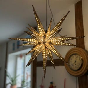 May include: A multi-pointed star-shaped pendant light fixture with a perforated surface pattern. The structure is composed of numerous triangular spikes radiating from a central core, emitting a warm glow through the small circular cutouts.