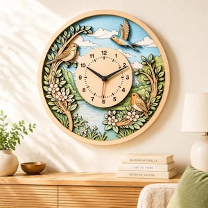 Op de afbeelding: Een ronde wandklok met een lichthouten frame met een gelaagde 3D-scène van een blauwe lucht, witte wolken, groene bomen en drie vogels. De centrale wijzerplaat is beige met zwarte cijfers, zwarte uren- en minutenwijzers en een rode secondewijzer.