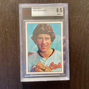 May include: A baseball card featuring Jim Palmer, a baseball player for the Baltimore Orioles. The card is graded 8.5 by Beckett Grading Services. The card is from the 1976 Topps set.