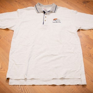 May include: White polo shirt with a navy blue trim and a small embroidered Denver Broncos logo on the chest.