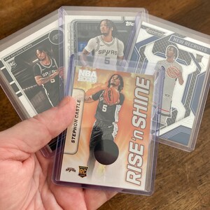 May include: A collection of four Stephon Castle basketball trading cards in protective plastic sleeves. The cards feature the San Antonio Spurs player in various uniforms, including a Rise 'n Shine card with a circular jersey patch insert.