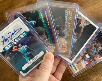 May include: A collection of five basketball trading cards featuring Larry Johnson, a former NBA player for the Charlotte Hornets. The cards are in protective plastic sleeves. The top card features a signature and the text "Great Significance".