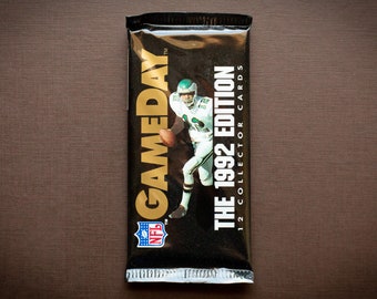 Puede incluir: Un paquete de tarjetas de colección de fútbol americano Gameday NFL de 1992 con un jugador de fútbol en uniforme verde. El paquete es negro con letras doradas y el logotipo de la NFL.