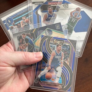 May include: A collection of basketball trading cards featuring Luka Dončić, held in protective sleeves. The cards showcase various designs and team logos, with a focus on the Dallas Mavericks and Lakers.